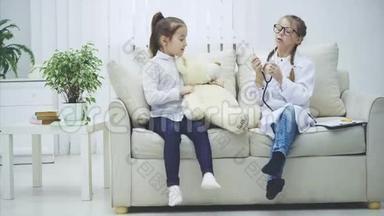 两个可爱的孩子在玩泰迪熊。 扮演医生的女孩正在用听诊器检查<strong>毛绒熊</strong>。